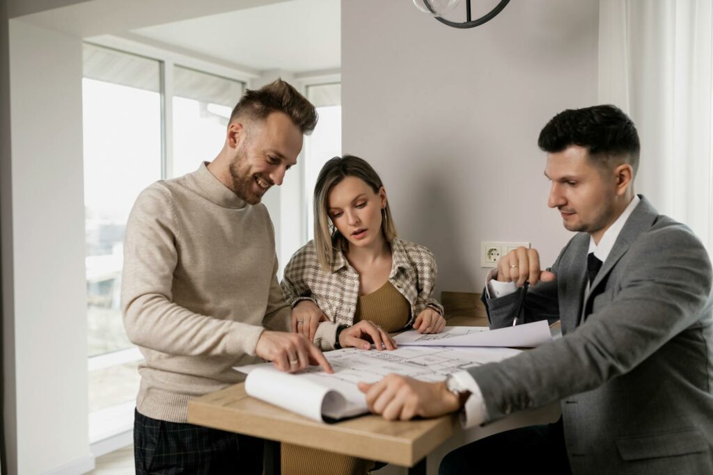 Three adults reviewing real estate blueprints indoors at a table.